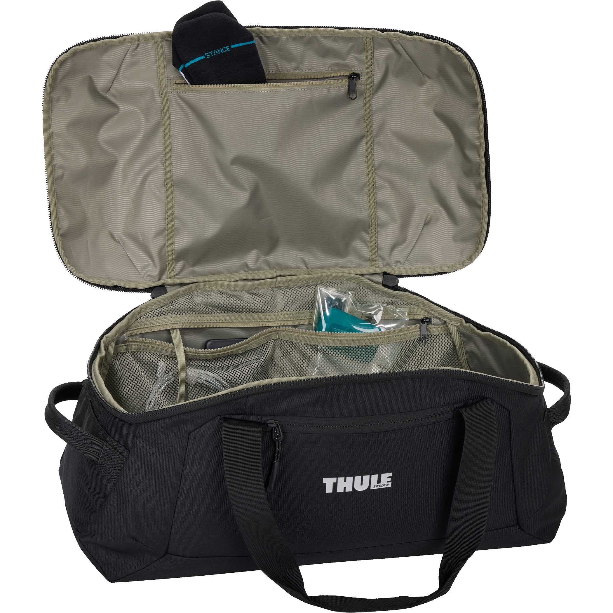 Thule Lumion Duffle in black recycled polyester material placed in a modern travel setting, shown as a spacious duffel bag with structured shape and front zippered pocket designed for organized packing and travel use.