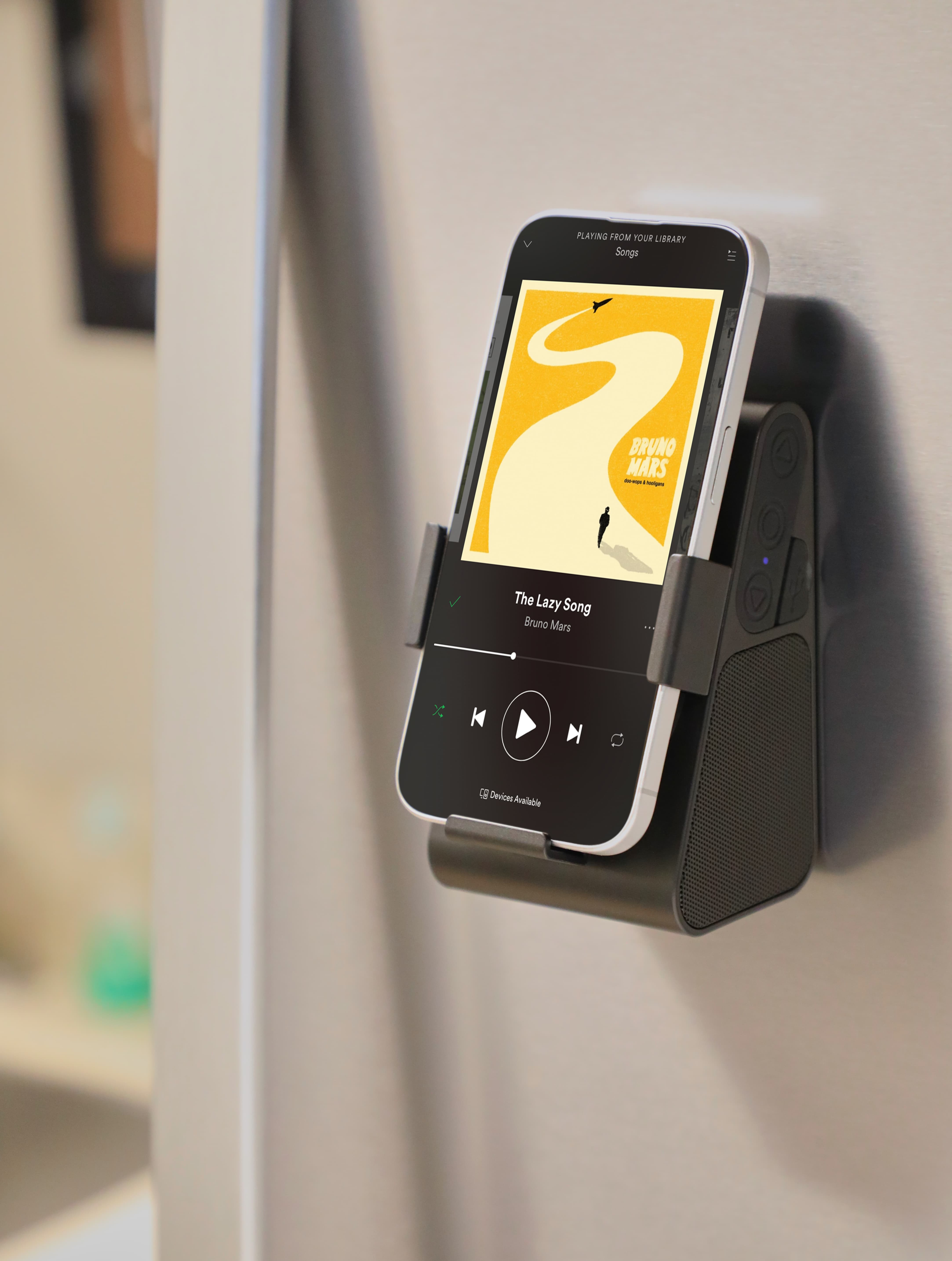 Phone Grip Outdoor Magnetic Bluetooth Speaker in black ABS plastic displayed in a close-up lifestyle setting, emphasizing the magnetic back securing it to metal and the compact design used for portable, hands-free listening.