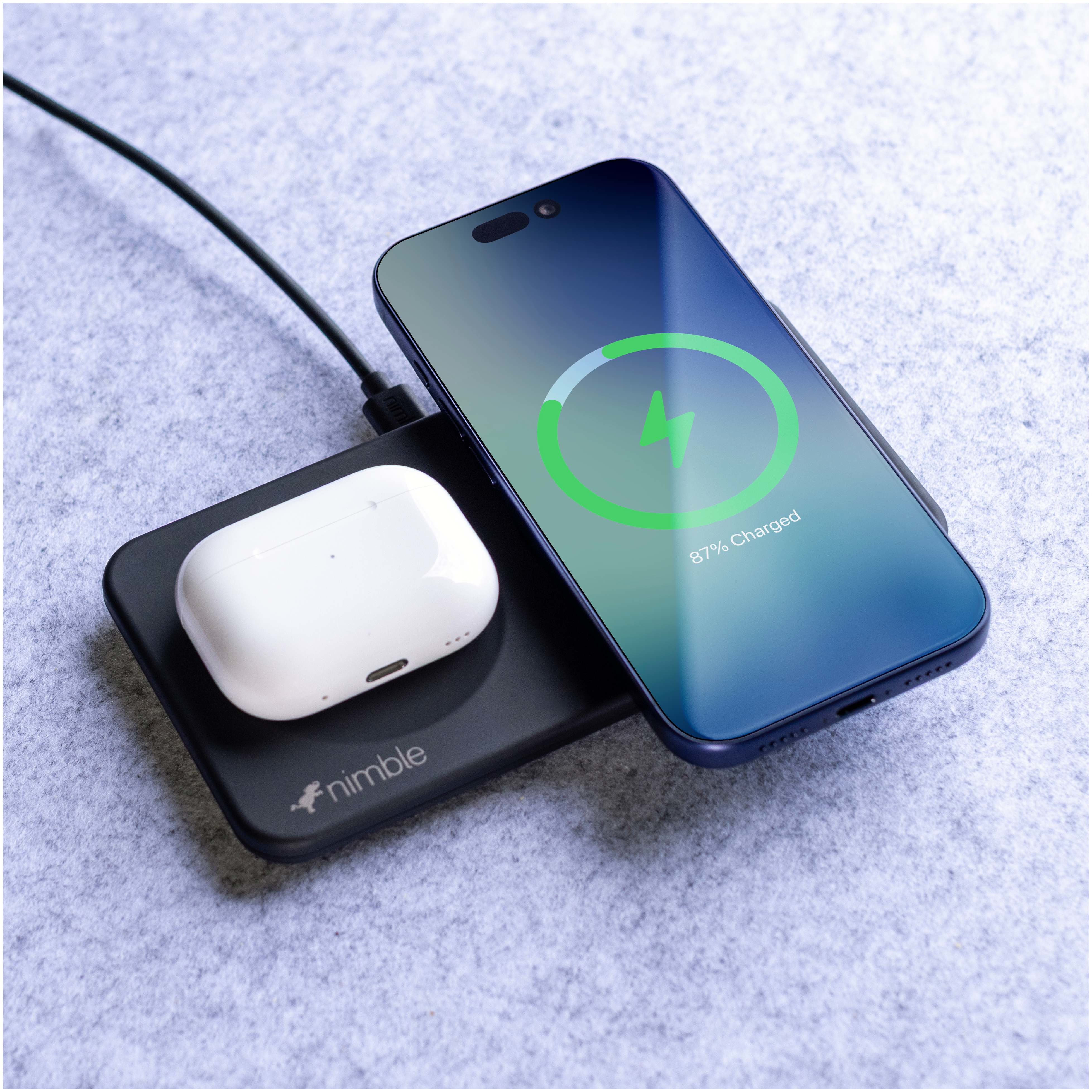 Nimble Podium 2-in-1 Wireless Charging Stand in black with matte finish, positioned on a modern wooden desk beside a laptop and office accessories, charging a smartphone in upright position for easy viewing and everyday workspace use.
