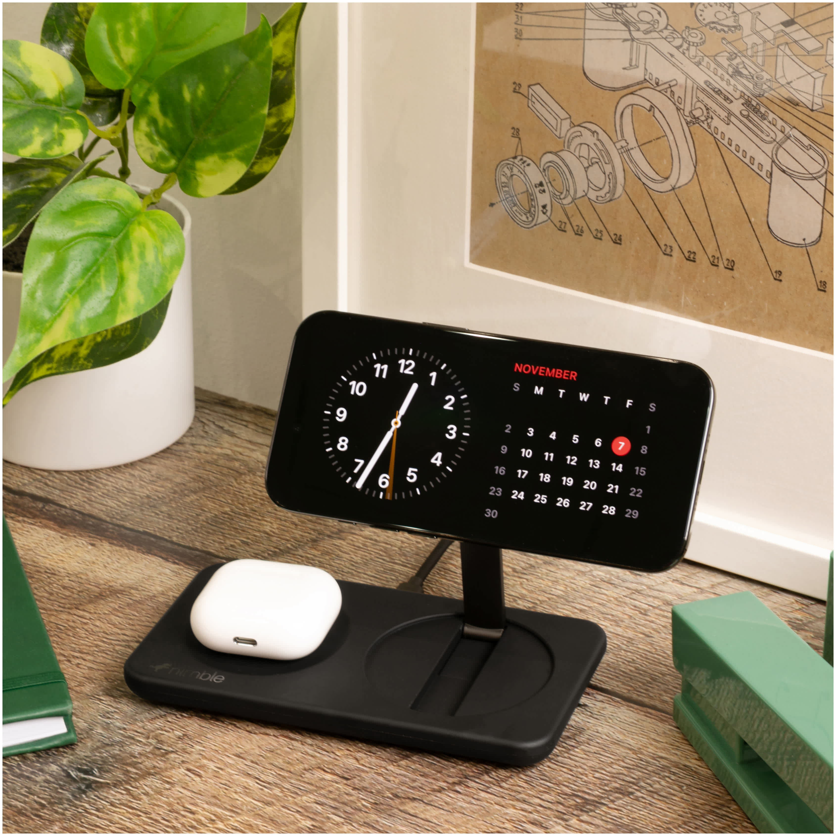 Nimble Podium 2-in-1 Wireless Charging Stand in black with compact base and vertical charging platform, placed on a bedside table next to a lamp and personal items, wirelessly charging a smartphone in a clean, minimal home setting.