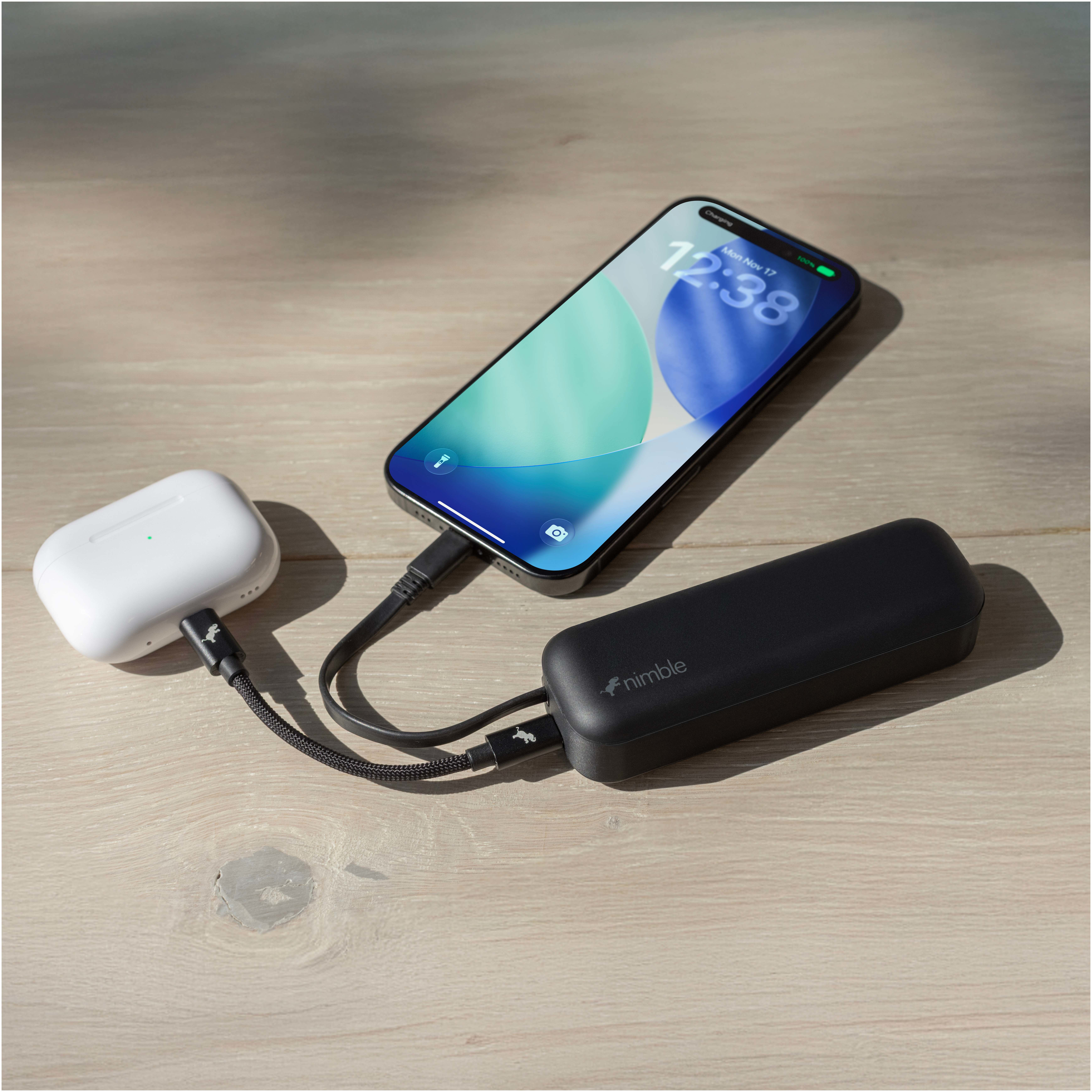 Black Nimble Wally Pro 20 5,000 mAh Power Bank and Wall Charger in black with compact rectangular design and folding AC prongs, plugged into a wall outlet in a modern home interior while charging a connected device on a nearby surface