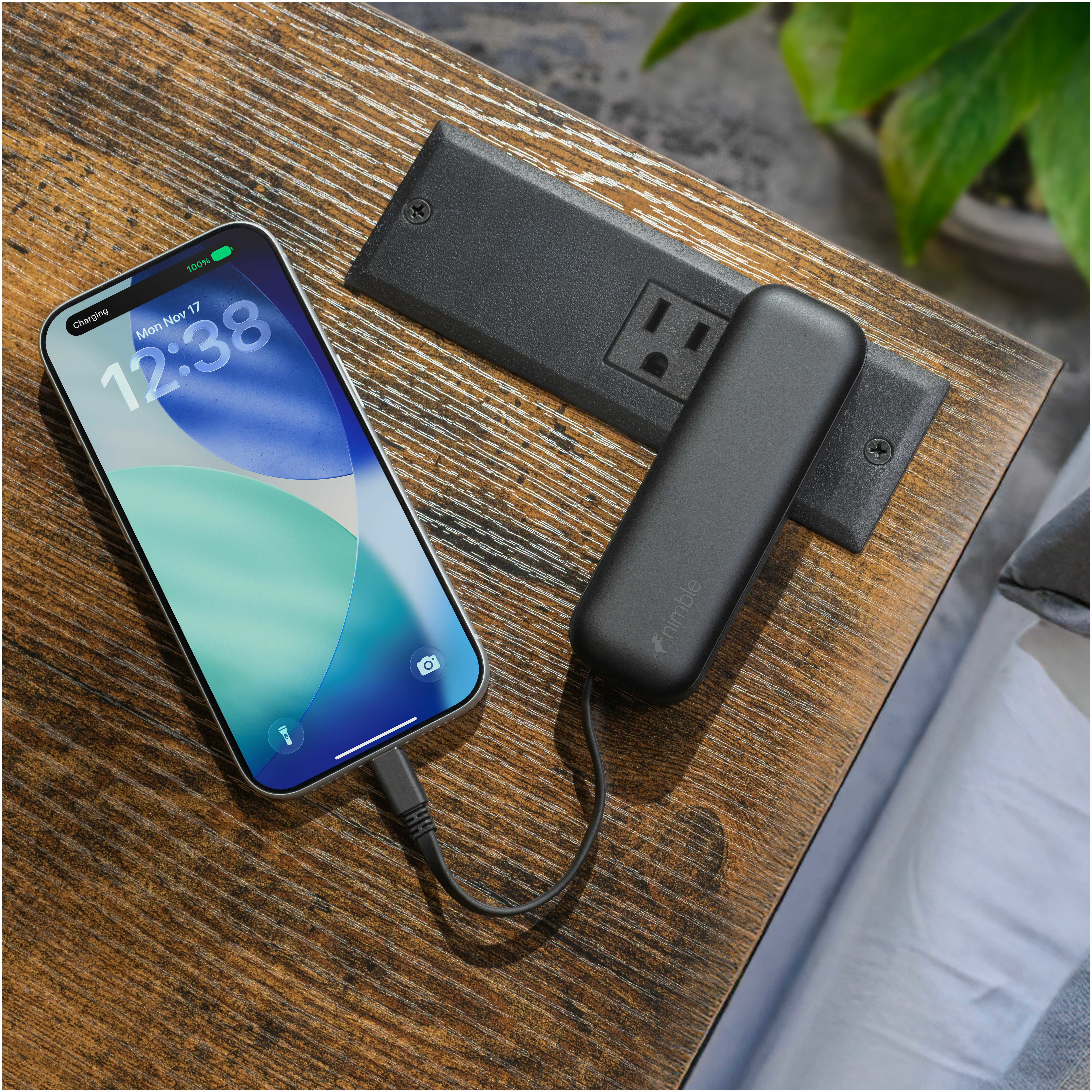 Black Nimble Wally Pro 20 5,000 mAh Power Bank and Wall Charger in black matte finish, shown being used in a travel or work setting with connected USB-C cable charging a smartphone on a desk, highlighting its portable charging and wall charging functionality.