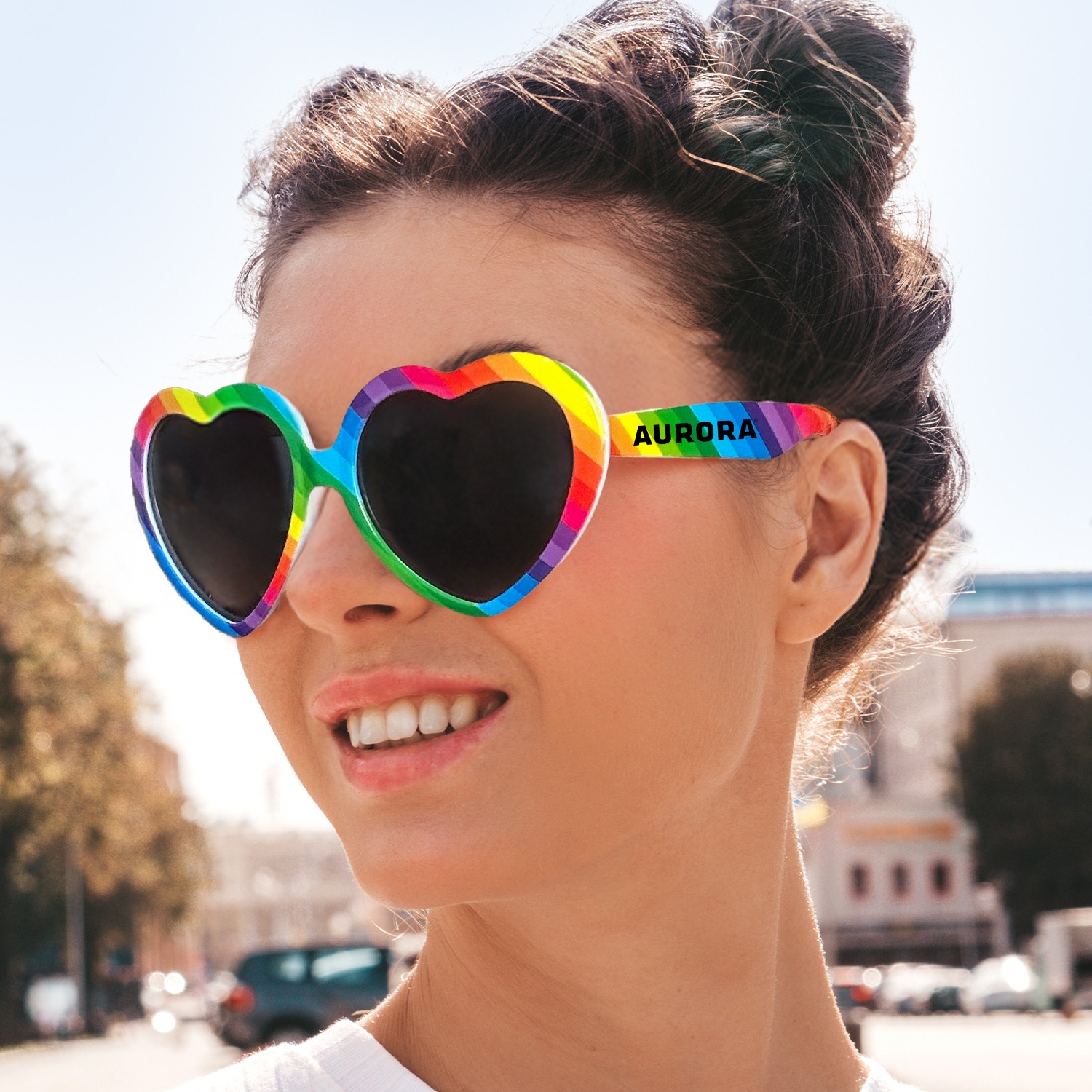 A woman wearing a Rainbow heart-shaped sunglasses made of lightweight polycarbonate plastic, featuring glossy translucent multicolor frames with UV-protective tinted lenses, designed as novelty eyewear for promotional events, parties, and outdoor use.