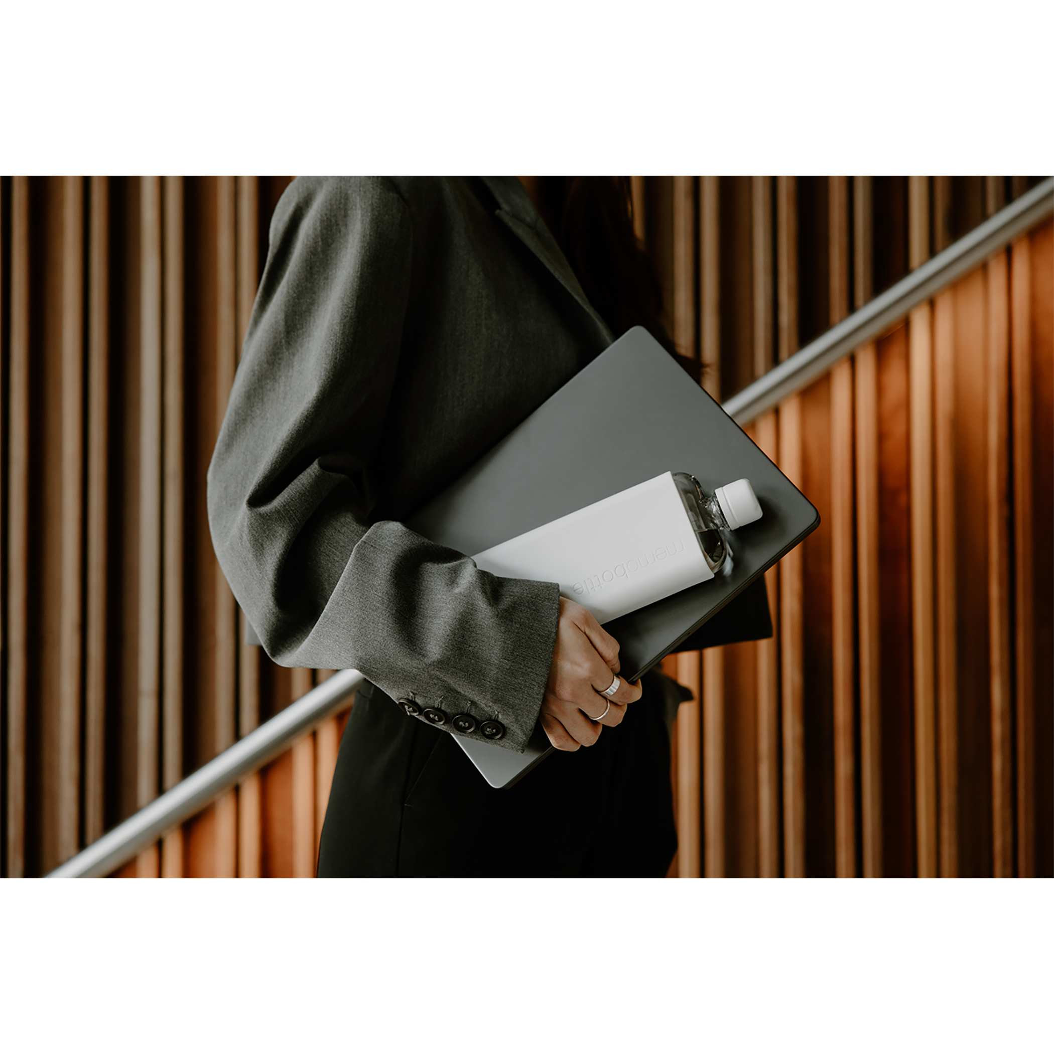 Gray Slim Original Colored memobottle™ 15 oz in flat, rectangular Tritan™ plastic with a silicone sleeves, displayed in a minimalist lifestyle setting, showing its flat for everyday carry, highlighting its space-saving slim profile intended for fitting into bags alongside laptops, books, or documents for portable hydration.