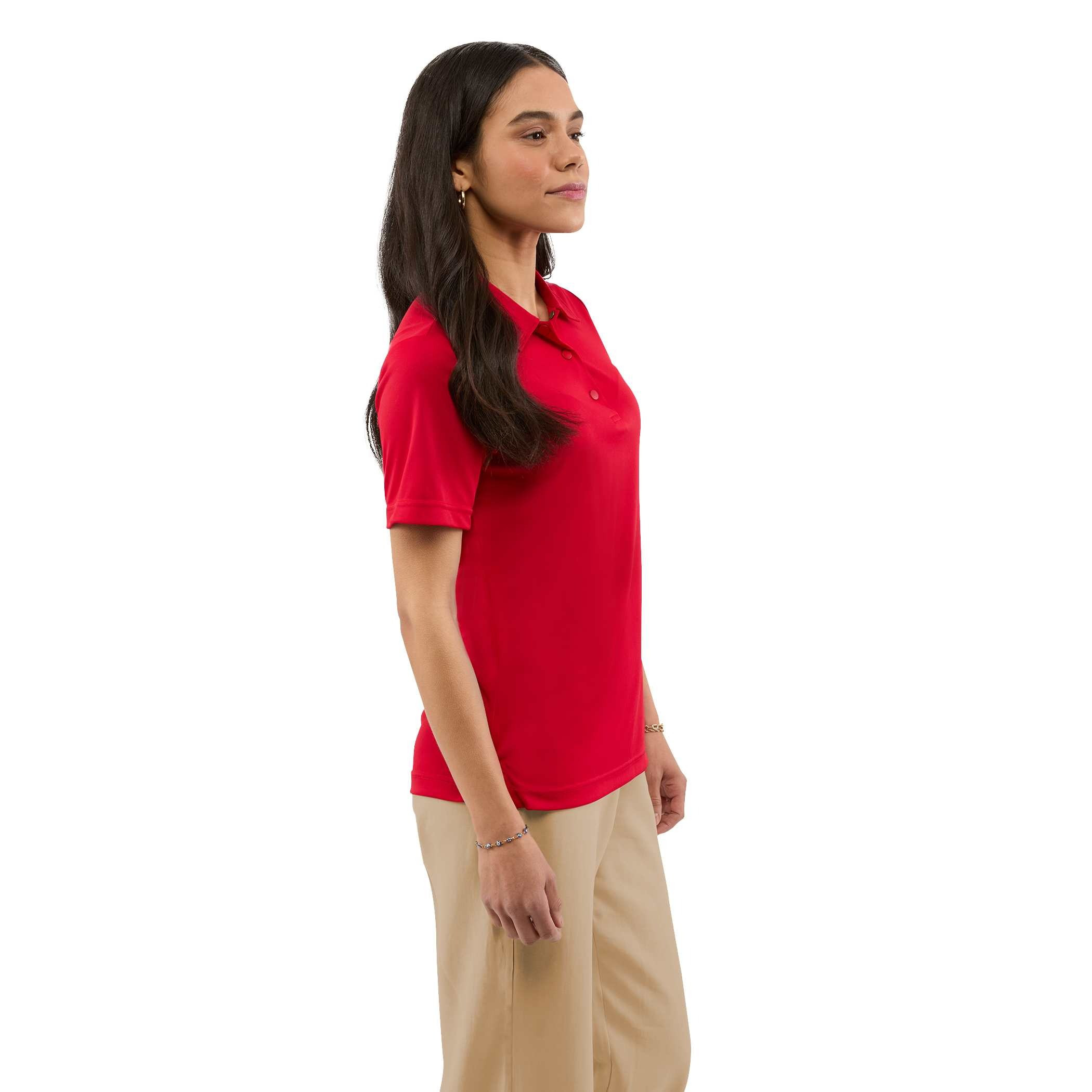 A woman wearing a Team Red Women’s Dara Recycled Tech Polo made from structured recycled polyester fabric during an outdoor event. The short-sleeve polo features a modern two-snap button placket, clean snag-resistant texture, and an athletic fit, showcasing its use as professional corporate apparel.