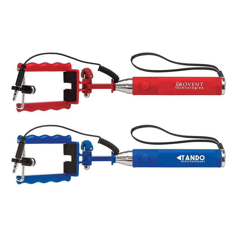 Red and Blue Snap Compact Selfie Stick, featuring a compact stainless steel telescoping handle with a ribbed silicone grip, spring-loaded smartphone clamp, wrist strap, and built-in shutter button for capturing selfies and group photos.