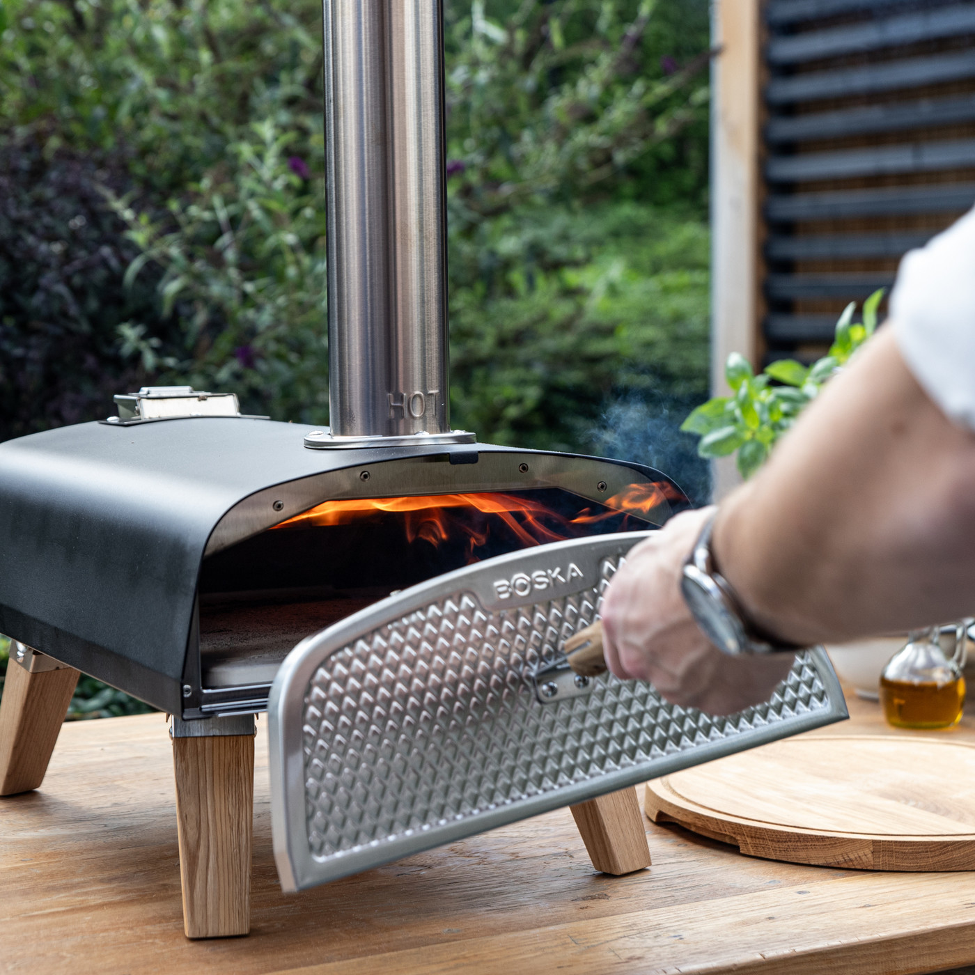 Black outdoor pizza oven with stainless steel construction and stylish European oak accents, designed for high-temperature wood pellet cooking and crispy homemade pizza.
