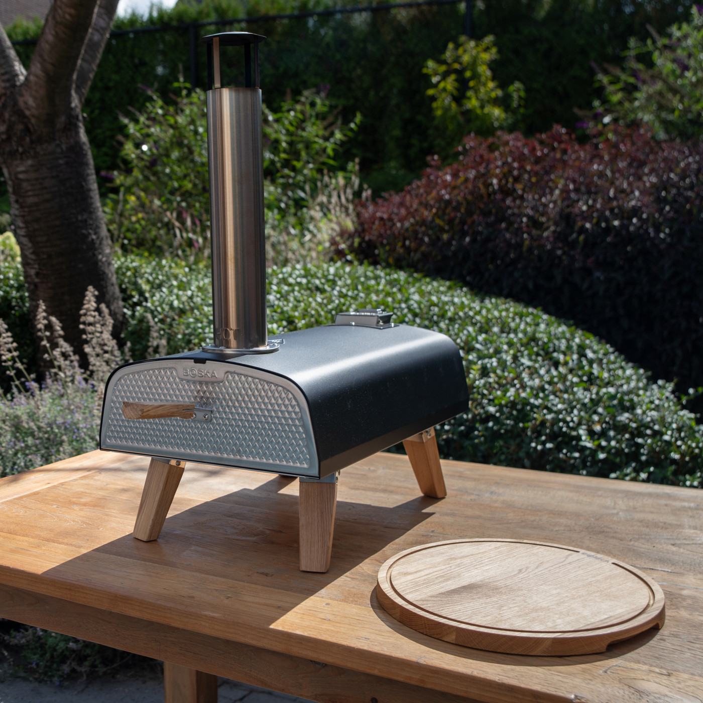 Black outdoor pizza oven with stainless steel construction and stylish European oak accents, designed for high-temperature wood pellet cooking and crispy homemade pizza.