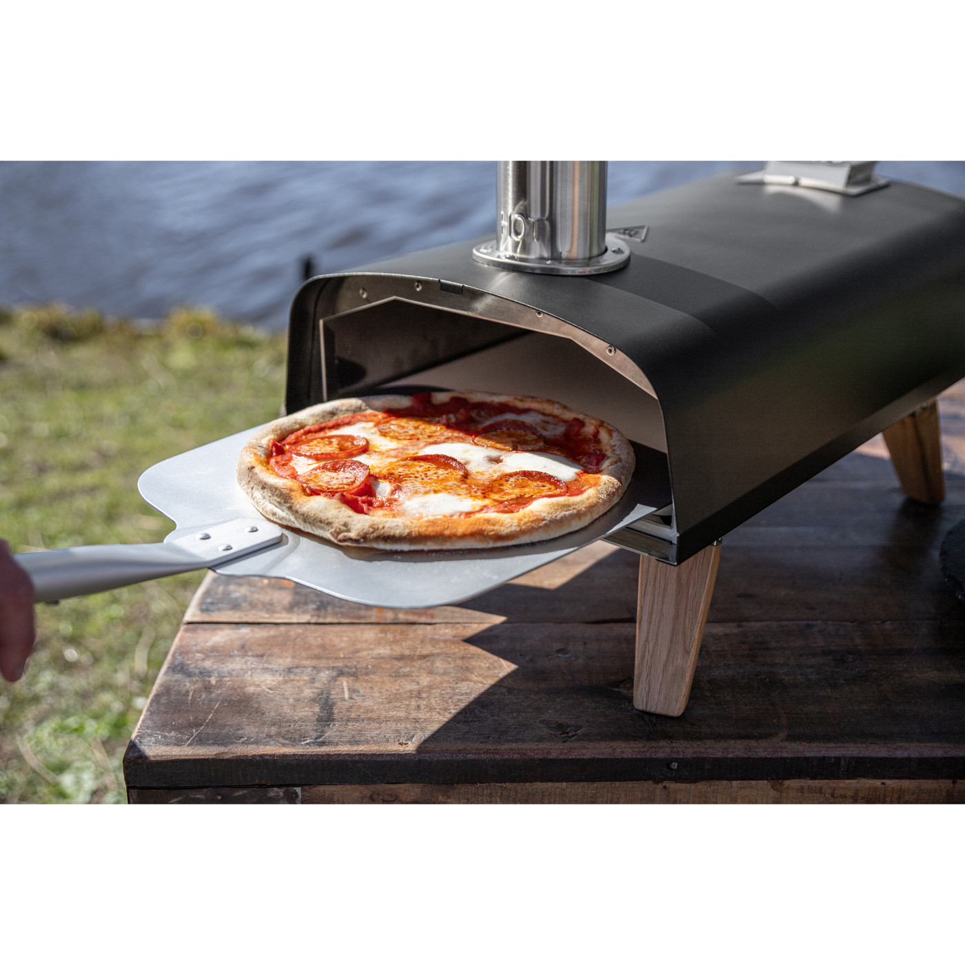 Black outdoor pizza oven with stainless steel construction and stylish European oak accents, designed for high-temperature wood pellet cooking and crispy homemade pizza.