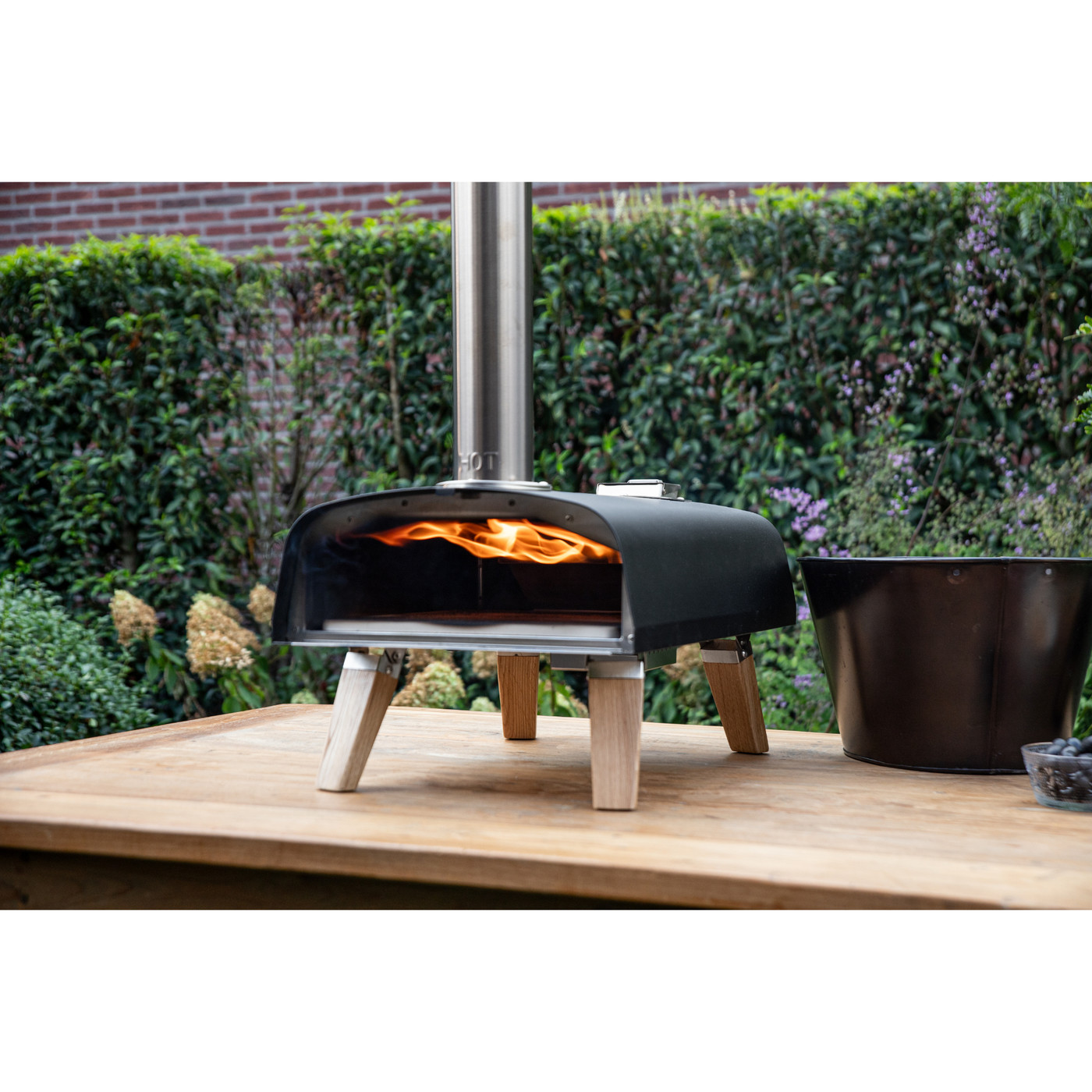 Black outdoor pizza oven with stainless steel construction and stylish European oak accents, designed for high-temperature wood pellet cooking and crispy homemade pizza.