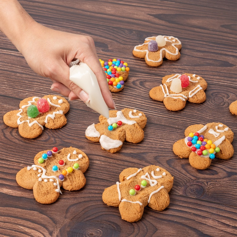 Gingerbread cookie decorating kit in a festive holiday house gift box with three gingerbread cookies, vanilla icing, and colorful candies for a fun seasonal activity.