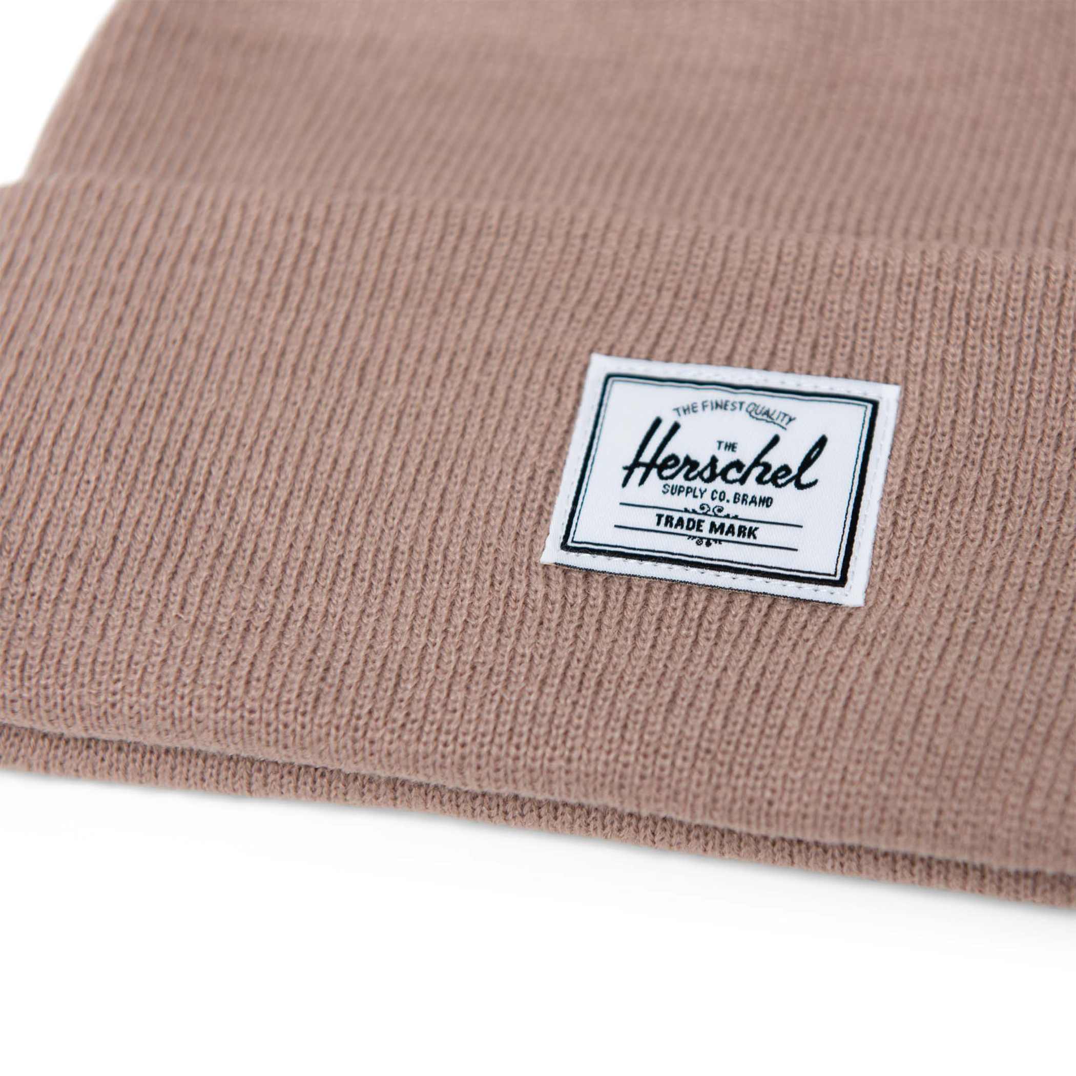 Close up of Herschel logo on Ash Rose Elmer beanie made from soft 100% acrylic, featuring a classic fit, a comfortable folded cuff, and an 8.25-inch-tall design for cozy cold-weather wear and custom logo branding.